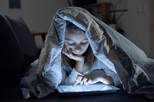 Young girl under duvet on tablet