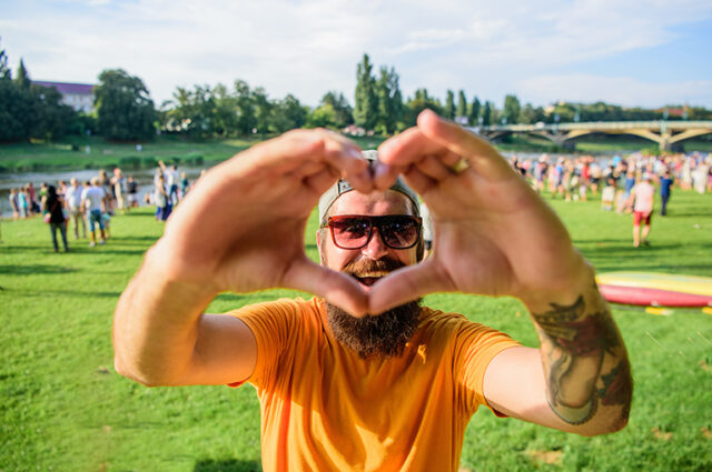 Hipster happy celebrate event picnic fest or festival. Cheerful fan love summer fest. Man bearded hipster in front of crowd people show heart gesture riverside background. Urban event celebration