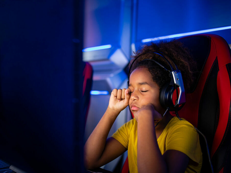 Child sat rubbing eyes while playing a computer game