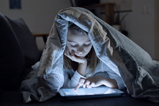 Girl using tablet under duvet at night