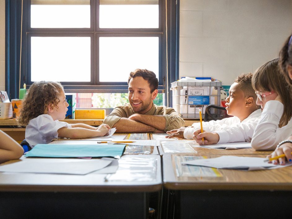 Male teacher listening to a pupil in a busy classroom